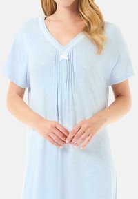 Un camisón azul claro de tejido suave que presenta un escote en V, mangas cortas, pliegues frontales y un pequeño lazo blanco en el escote.