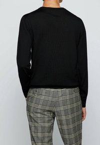 Svart ribbad tröja med långa ärmar och rundad halsringning. Kombinerad med grå rutiga byxor med krämfärgade ränder och knäppning.