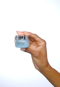 Petit pot bleu givré avec un couvercle argenté, étiqueté "Gel Hydratant pour les Yeux Hyaluronique Drench Water", tenu dans une main.