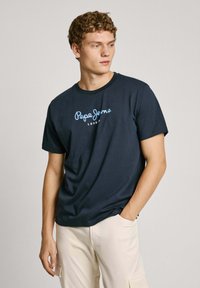 Tumši zila kokvilnas T-krekls ar īsām piedurknēm un apaļu kakla izgriezumu. Krūtīs ir gaiši zils "Pepe Jeans London" logo.