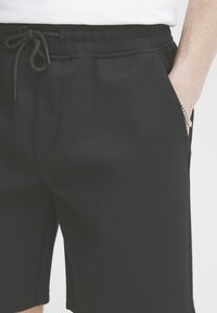 Shorts noirs en tissu texturé, dotés d'une taille élastique avec cordon de serrage, de poches latérales et d'une coupe décontractée.