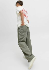 Casual outfit met een wit t-shirt met rode grafische print en losse olijfgroene broek, gecombineerd met witte sneakers.