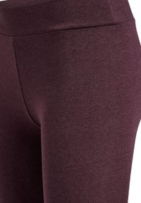 Bordeaux leggings met een gladde textuur, hoge tailleband en een aansluitend ontwerp, dat een effen kleur zonder patronen of accenten toont.