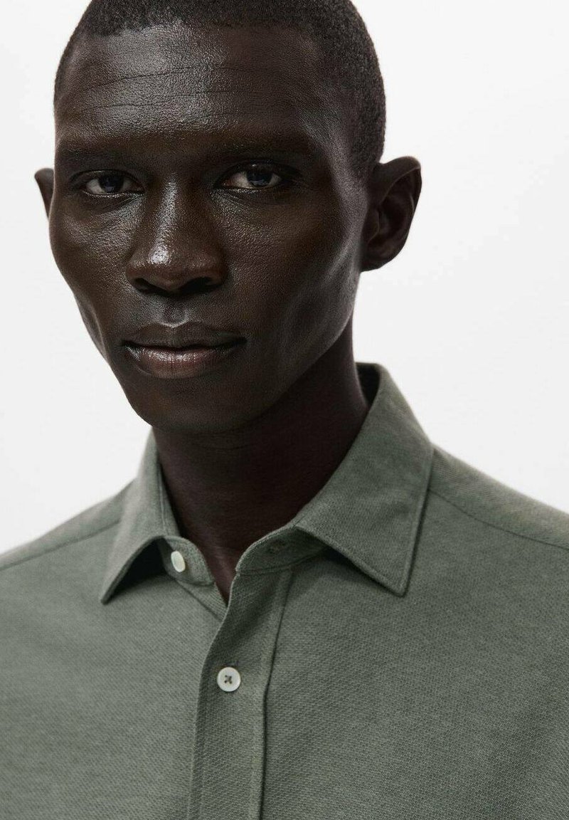 Grøn knap-op skjorte med en tekstureret finish, prydet med en spids krave og to knapper ved halsen. Enkel, moderne design uden mønstre.