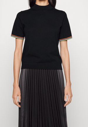Haut noir à manches courtes avec un col haut, mettant en valeur des rayures multicolores sur les manches. Porté avec une jupe plissée noire.