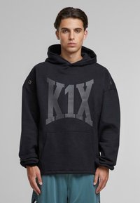 Czarna bluza z kapturem z dużym szarym logiem "K1X". Posiada kieszeń z przodu, sznurek do regulacji kaptura oraz metalowe oczka na rękawach.