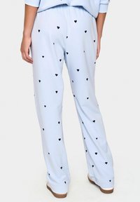 Pantaloni del pigiama azzurro chiaro dal tessuto morbido, con un motivo a cuori neri in tutto il capo. Vita elastica e design largo.