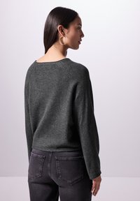 Grauer, gestrickter Pullover in lockerer Passform mit weitem Ausschnitt und langen Ärmeln. Kombiniert mit dunklen, eng anliegenden Jeans.