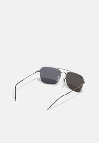 Ochelari de soare din metal cu un design elegant și unghiular. Lentile de un gri închis cu un gradient subtil, rame subțiri din argint și suporturi pentru nas transparente.