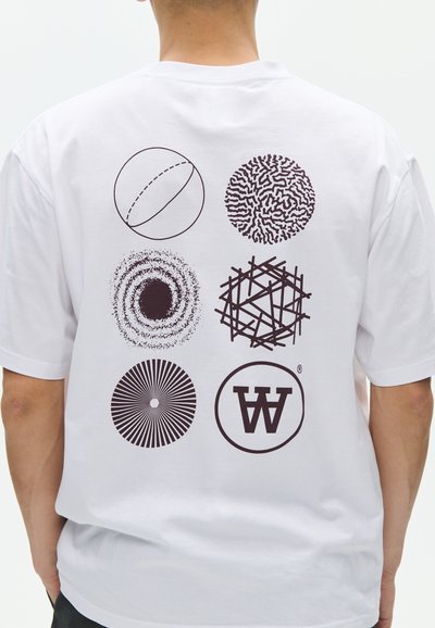 Dos d'un T-shirt blanc avec six motifs circulaires abstraits noirs disposés en deux colonnes et trois rangées, porté par une personne de dos.
