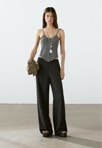 Svarta vida byxor med en texturerad, silverfärgad stickad croptop. Modellen håller en brun mockaklutch. Lång silverfärgad hängehalsband bärs.