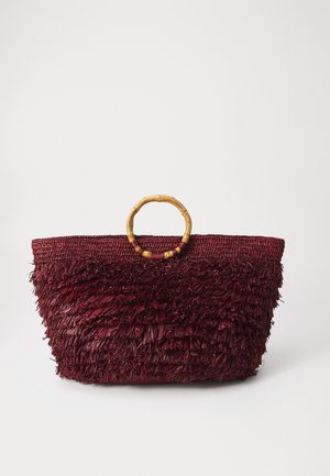 Sac à main tissé bordeaux profond avec franges texturées et poignées rondes en bois sur fond blanc uni.