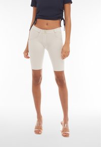 Shorts de bicicleta de talle alto en color beige, confeccionados con material elástico y diseño ceñido, que cuentan con dos bolsillos frontales y un cierre de doble botón.