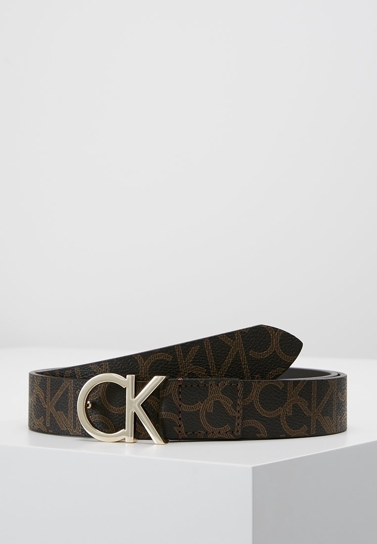 Ceinture de créateur noire et marron avec un motif répétitif "CK" et une boucle argentée "CK", présentée sur une surface blanche.