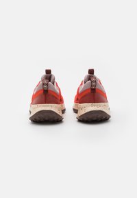 Scarpe da atletica rosse e grigie con tomaia in rete, suola leggera marrone chiaro con una texture e macchie scure. Linguetta sul tallone con marchio circolare.