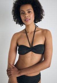 Črn bandeau bikini top s zasukanim sprednjim delom, nastavljivimi tankimi naramnicami in ujemajočimi se nizkimi hlačkami, ki imajo subtilen kovinski sijaj.