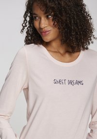 Long-sleeve, light pink t-shirt made of soft fabric featuring navy blue "SWEET DREAMS" text embroidered on the front.