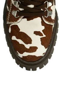 Botte en cuir de vachette brun et blanc avec une texture, dotée d'une semelle noire robuste, de œillets en métal et de lacets marron.