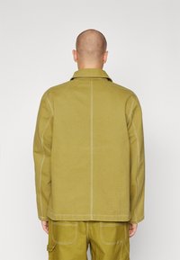 Chaqueta verde oliva con un cuello estructurado, costuras visibles y un corte relajado. El tejido parece duradero y tiene una textura suave.