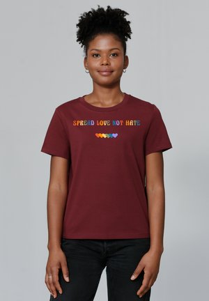 T-shirt en coton bordeaux à manches courtes, arborant le texte "RÉPANDRE L'AMOUR, PAS LA HAINE" en lettres multicolores au-dessus d'un motif en forme de cœur.