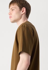 Braunes Baumwoll-T-Shirt mit kurzen Ärmeln, Rundhalsausschnitt und lockerer Passform. Der Stoff hat eine glatte Textur mit minimalen Nähten.