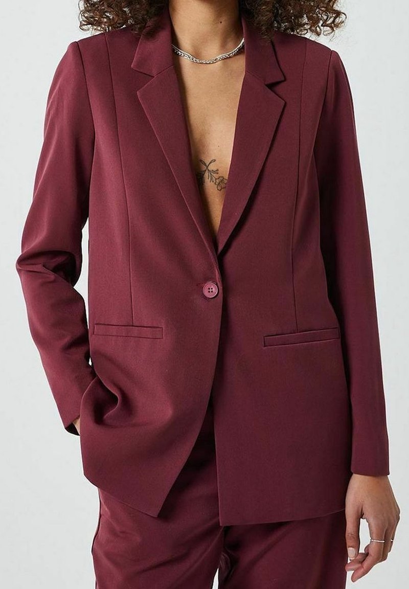 Blazer bordeaux cintré avec une fermeture à un seul bouton, des revers crantés, deux poches avant et une texture lisse.