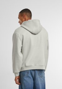 Lichtgrijze hoodie met een grote, verstelbare capuchon, met een relaxte fit en een zachte textuur. Zichtbare zijnaad en minimalistische ontwerpelementen.