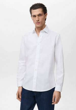 Weißes langärmliges Hemd aus glattem Baumwollstoff, mit klassischem Kragen und geradem Saum, kombiniert mit dunklen Denim-Jeans.