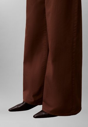 Bruine broek met wijde pijpen gemaakt van gladde stof, gecombineerd met puntige zwarte enkellaarsjes, die een moderne silhouet vastleggen.