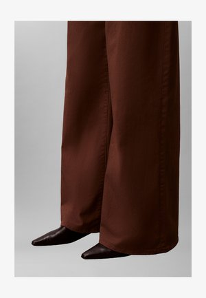 Bruine broek met wijde pijpen gemaakt van gladde stof, gecombineerd met puntige zwarte enkellaarsjes, die een moderne silhouet vastleggen.