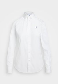 Camisa blanca de manga larga con cuello abotonado, que presenta un pequeño logotipo bordado en navy en el lado izquierdo del pecho y una textura de algodón suave.