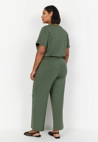 Completo a due pezzi verde oliva composto da una maglietta a maniche corte dal taglio morbido e pantaloni a gamba larga, realizzato in tessuto morbido. I sandali hanno un design a rete.
