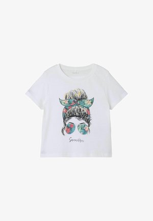 T-shirt en coton blanc avec un design graphique représentant une femme avec un chignon et un serre-tête floral, portant des lunettes de soleil entourée de feuilles tropicales et de fleurs.