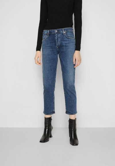 Blaue Denim-Jeans mit einem verkürzten Schnitt, geradem Schnitt und ausgefransten Säumen, kombiniert mit schwarzen Leder-Stiefeletten.