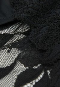 Zwart kant met bloemmotieven en ingewikkelde texturen, gelaagd over een doorschijnende gaasachtergrond, wat diepte en elegantie creëert.