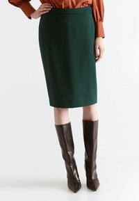 Vihreä kynähame, joka on valmistettu sileästä kankaasta ja siinä on vartaloa myötäilevä malli vyötäröllä oleva vyö.