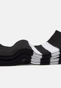 Black socks with white stripes, featuring a ribbed texture and a soft-knit design, stacked in a wave shape.