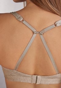 Soutien-gorge en tissu texturé beige, doté d'un design à dos croisé et de bretelles réglables. Comprend une fermeture à crochets et œillets à l'arrière.