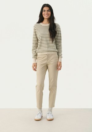 Pull rayé beige et olive, avec des poignets côtelés ; accompagné d'un pantalon beige et de baskets blanches. Design simple et coupe décontractée.