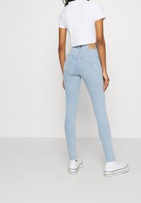 Ljusblå tajta jeans i denim, med hög midja, femficksdesign och en brun läderpatch på baksidan.