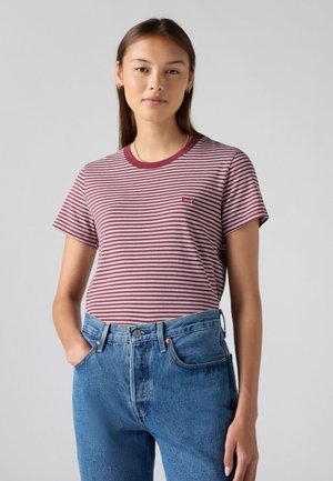 T-shirt à rayures rouges et blanches avec col ras du cou et manches courtes ; arbore un petit logo rouge Levi's sur le devant. Porté avec un jean taille haute bleu.