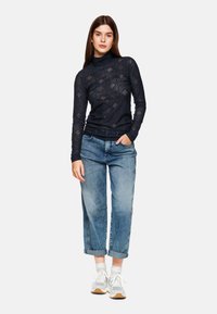 Marineblaues Spitzen-Turtleneck-Oberteil mit einem strukturierten Muster, kombiniert mit hellblauen Denim-Jeans mit umgeschlagenen Bündchen und weißen Sneakers.