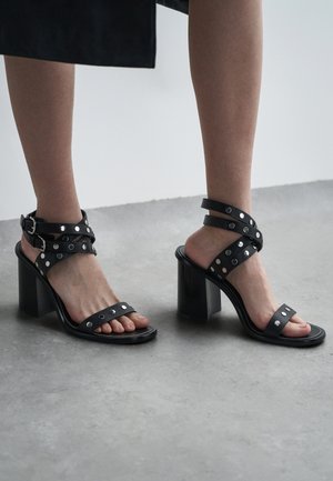 Sandale negre cu toc, cu mai multe curele; puseuri de metal argintiu ca accente; toc bloc glossy, elegant; design cu vârf deschis; textură de piele netedă.