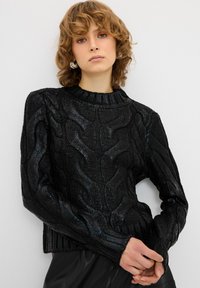 Schwarzer Strukturpullover mit einem gerippten Kragen und Bündchen. Verfügt über ein strukturiertes Muster und ein kurzes Design. Weiches, grob gestricktes Material.