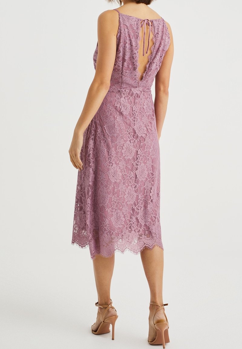 Krajkové šaty v světle fialové barvě s vroubkovaným lemem, výstřihem do V na zádech a zavazovacími ramínky. Látka je zdobena květinovými vzory a má přiléhavý střih.