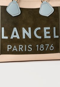 Καφέ και μπεζ δερμάτινη τσάντα χειρός με μπλε δερμάτινες λαβές και κεντημένα γράμματα «LANCEL PARIS 1876» στο μπροστινό πάνελ.