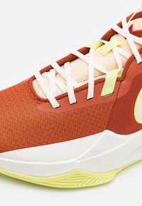 Czerwono-pomarańczowy teksturowany sneaker z białymi sznurówkami, kontrastującymi żółtymi akcentami i gładką białą podeszwą z wzorem w zygzak.