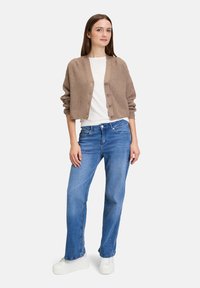 Ljusbrun ribbad cardigan med knappstängning, bärs över en vit skjorta, ihop med blå jeans och vita platåskor.