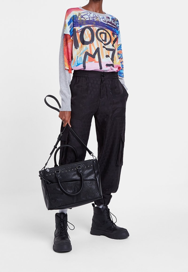 Grafisch tops met lange mouwen met kleurrijke ontwerpen, gecombineerd met zwarte cargobroeken. Zwarte textuurhandtas en stevige zwarte laarzen maken de outfit compleet.