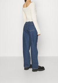 Haut long à manches longues en tricot blanc avec un dos ouvert, associé à un jean bleu à jambes larges. Chaussures à plateforme noires. Design simple, tissu texturé.